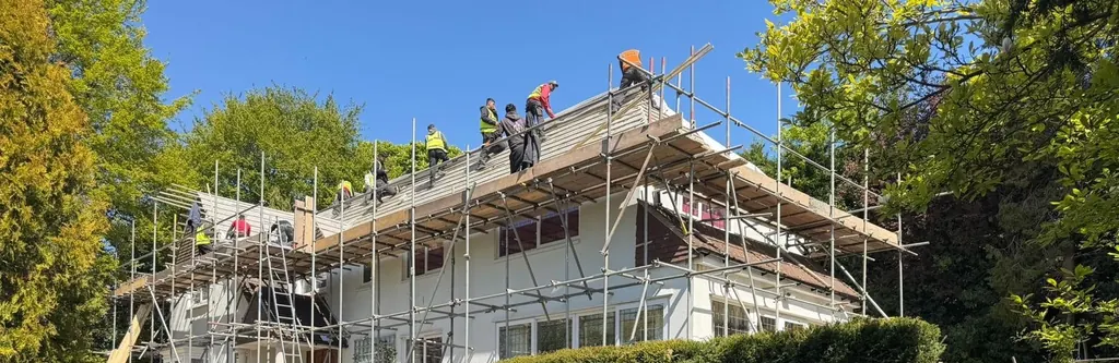 Roofing crew on a scaffolded white house beneath blue sky