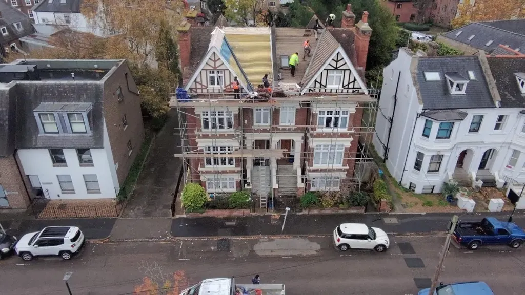 Elevated view of roofers on a large gabled house under scaffold