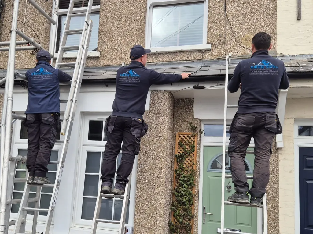 Three roofers on ladders fitting a gutter below a window