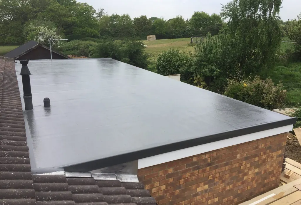 Dark flat roof with vent pipes beside a green garden