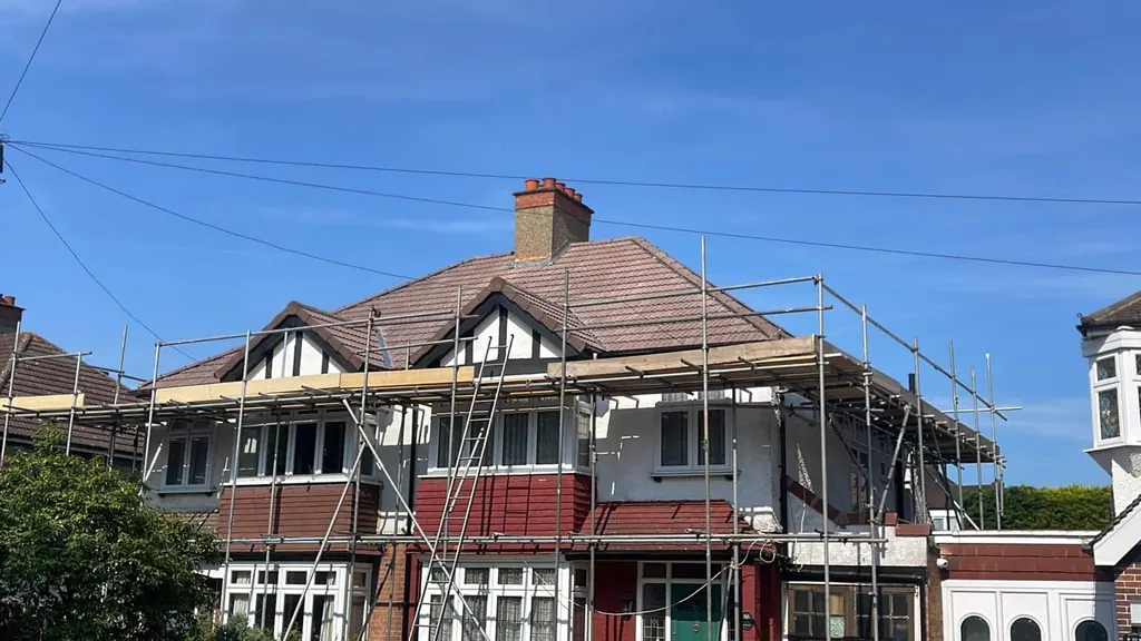 Tiled hipped roof on a scaffolded semi beneath blue sky