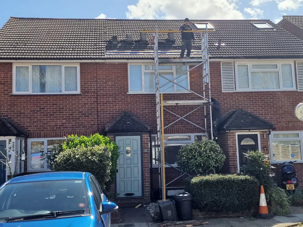 Roofer on a scaffold tower at the eaves of a tiled terrace
